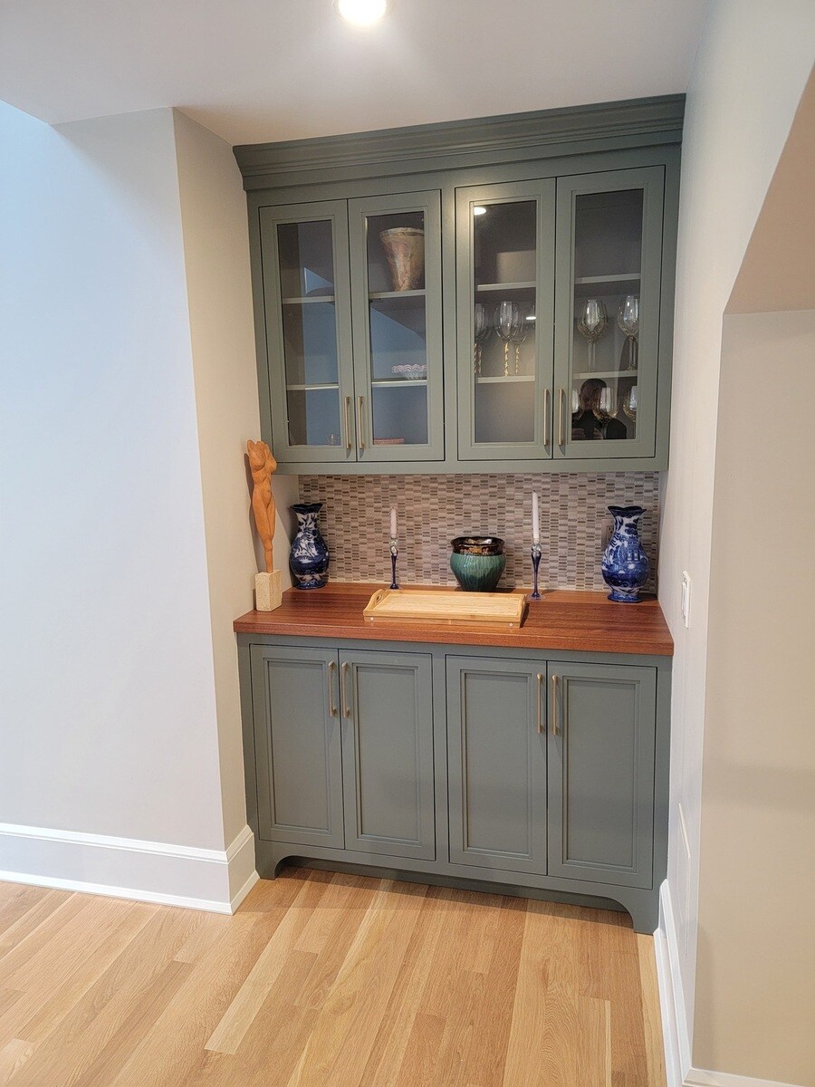 A home bar featuring dark green cabinets, warm wood countertops, and decorative accents, in an Acton, MA renovation by Thomas Buckborough & Associates