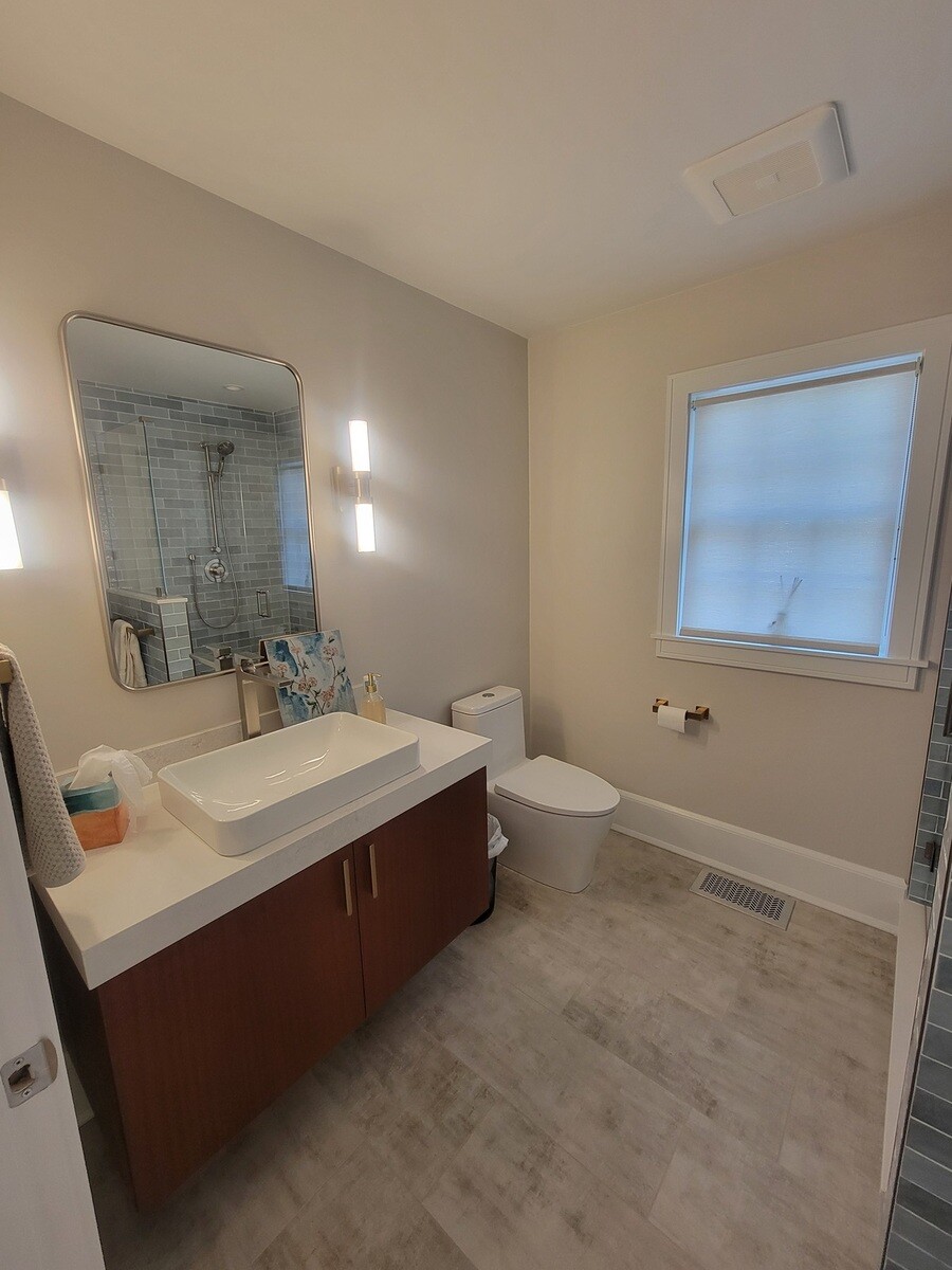 Modern bathroom design with a minimalist wood vanity, large mirror, and elegant lighting by Thomas Buckborough & Associates