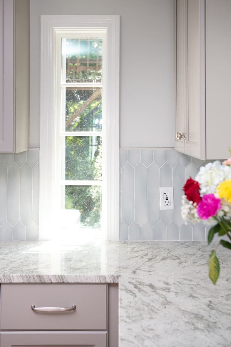 A modern kitchen renovation with a narrow window, natural light, and decorative tile backsplash by Thomas Buckborough & Associates