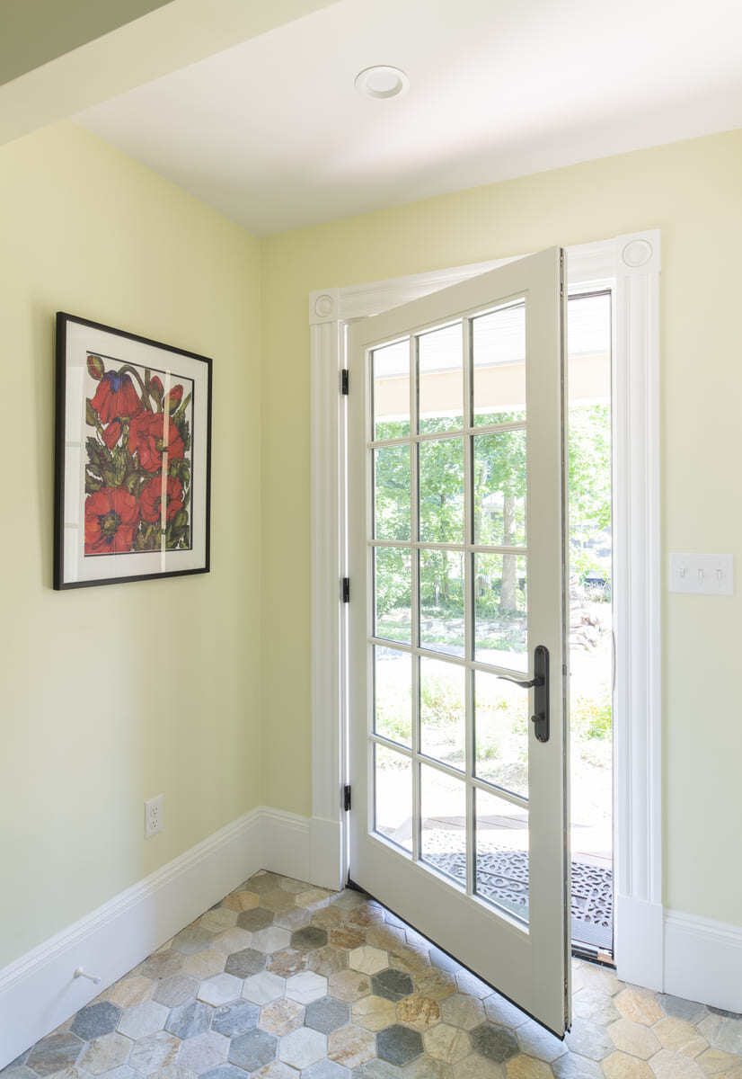 Light-filled entryway with a French door, hexagon tile flooring, and a floral artwork in an Acton, MA home remodel by Thomas Buckborough & Associates