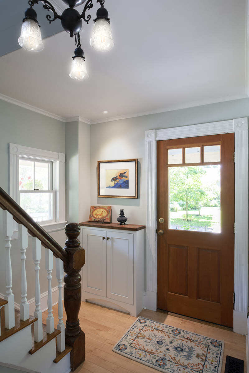 Welcoming home entryway featuring a wooden door, staircase with white balusters, and vintage-inspired lighting in an Acton, MA remodel