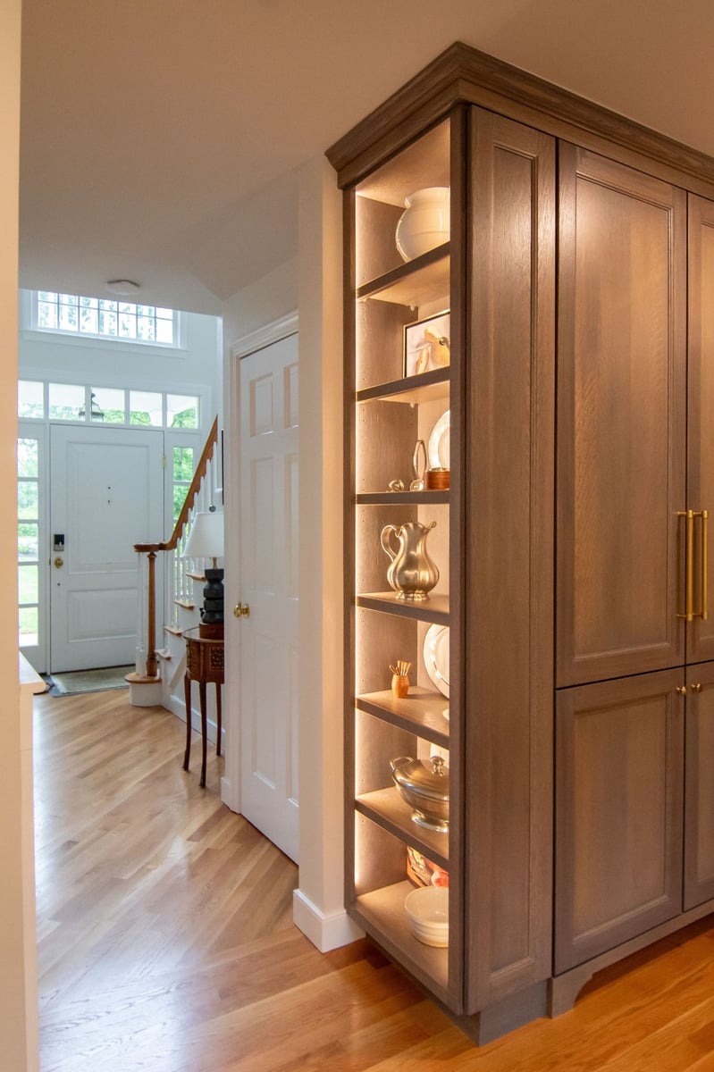 Glass-front cabinet with stacked neutral dishware above a white quartz counter and small potted plants. (1)