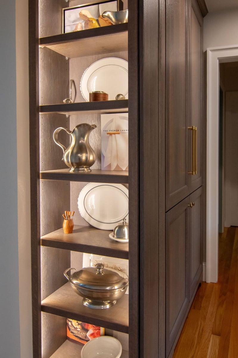 Glass-front cabinet with stacked neutral dishware above a white quartz counter and small potted plants. (2)