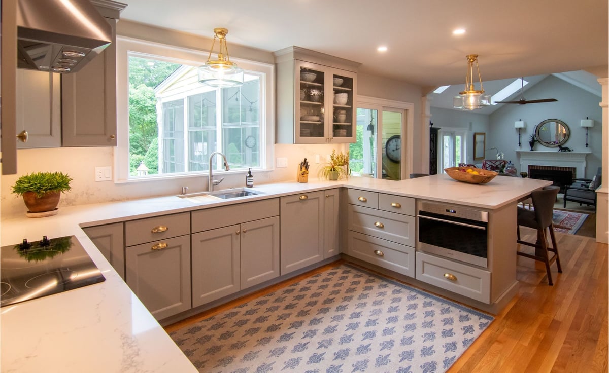 Modern gray kitchen with shaker cabinets, white quartz countertops, and a large island, opening into a bright living room.
